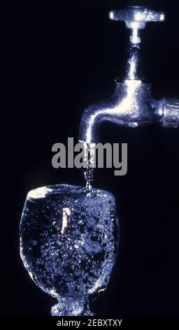 EAU D'UN ROBINET EN ARGENT À L'ANCIENNE COURANT DANS UN VERRE Banque D'Images