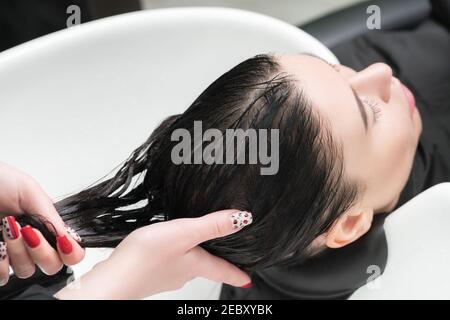 Les mains du coiffeur se laver les cheveux longs de la femme brune avec du shampooing dans un évier spécial pour le shampooing dans un salon de coiffure Banque D'Images