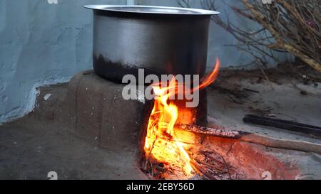 Feu de bois rougeâtre illuminant dans poêle en argile dans la cuisine indienne traditionnelle. Flammes rouges de feu dans poêle en brique avec poêle en aluminium. Banque D'Images