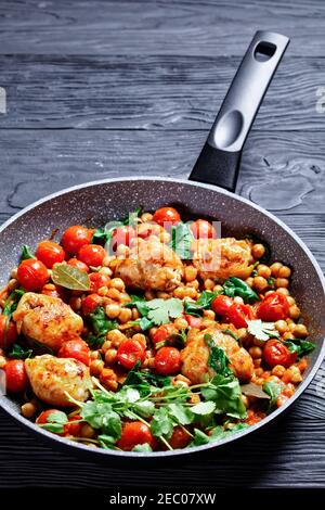 Curry traditionnel de poulet et de pois chiches de cuisses de poulet désossées avec tomates cerises, épinards, gingembre, servi avec de la coriandre fraîche sur une poêle o Banque D'Images