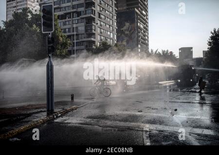 Santiago, Chili. 12 février 2021. Un cycliste s'échappe alors que la police lance un canon à eau dans les rues lors de manifestations contre la brutalité policière à Santiago. Plusieurs manifestants sont descendus dans la rue pour protester contre le gouvernement du président Sebastian Pinera, en attaquant et en brûlant un véhicule de police, blessant ainsi un officier à la suite du décès d'un artiste de rue qui a été abattu par la police dans la ville de Panguipulli après avoir refusé de coopérer avec une fouille policière. Crédit : SOPA Images Limited/Alamy Live News Banque D'Images