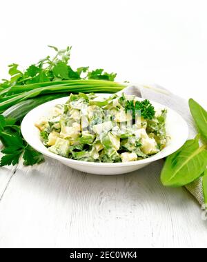 Salade de concombre, d'ostrel, de pommes de terre bouillies, d'œufs et d'herbes, garnie de mayonnaise dans une assiette blanche, de persil, d'oignons verts et d'une serviette de cuisine Banque D'Images