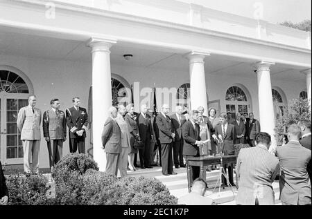 Cérémonie d'assermentation, général Maxwell Taylor, Président, JCS, 12 h 00. Le président John F. Kennedy (au centre à droite, à micros) prononce des remarques lors de la cérémonie d'assermentation du général Maxwell D. Taylor en tant que président des chefs d'état-major interarmées (JCS); le général Taylor et le procureur général, Robert F. Kennedy, se tiennent à droite du président Kennedy. En regardant les marches de la Colonnade de l'aile Ouest, en commençant à l'extrême gauche (de gauche à droite): Aide militaire au président, le général Chester V. Clifton; aide aérienne au président, le général de brigade Godfrey T. McHugh; aide navale au président, le capitaine Banque D'Images