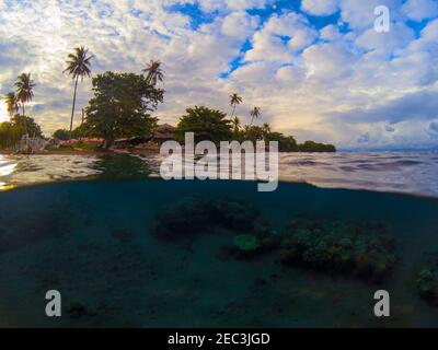 Photo partagée avec île tropicale et récif de corail sous-marin. Double paysage avec mer et ciel. Au-dessus et au-dessous de la ligne de flottaison dans la mer tropicale. Coucher de soleil Banque D'Images