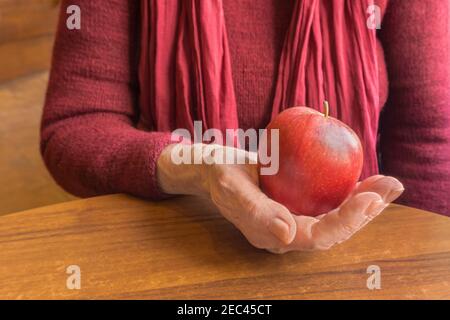 Pomme juteuse rouge dans les vieilles mains froissées de femmes âgées en rouge, gros plan Banque D'Images