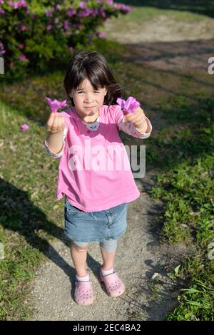 Petite fille vêtue de rose avec un plâtre sur son genou tenant des fleurs roses.Printemps. Banque D'Images