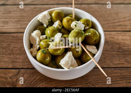 Bol d'olives vertes saines et fromage feta servi avec des cure-dents en apéritif ou en entrée vus sous un angle élevé sur une table en bois Banque D'Images