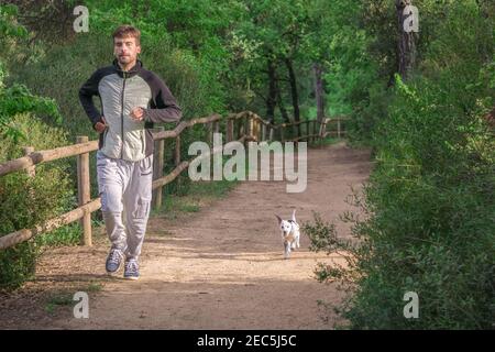 Homme sportif qui court rapidement avec son chien sur le sentier du parc des arbres verts dans l'après-midi. Concept de mode de vie sain.. Banque D'Images