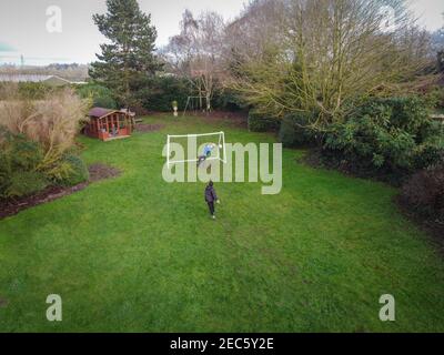 Vue sur un jardin à l'arrière d'une maison de campagne anglaise, montrant des enfants jouant au football par une journée ensoleillée. Banque D'Images