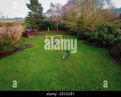 Vue sur un jardin à l'arrière d'une maison de campagne anglaise, montrant des enfants jouant au football par une journée ensoleillée. Banque D'Images