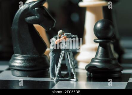 Figurines miniatures de cameraman et d'échecs à bord. Filmer le jeu de checkmate. Chevalier noir et pion dans l'appareil photo. Nouvelles sur les échecs. Vidéographe Banque D'Images
