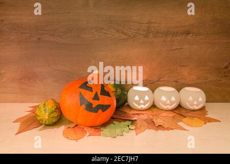 Décoration d'Halloween têtes de citrouille colorées, lanternes en forme de courge brûlantes, et feuilles d'automne sèches sur fond de bois. Concept Halloween. Banque D'Images