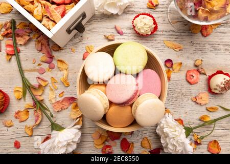 Couche plate de macarons français colorés dans un bol avec pétales et des fleurs Banque D'Images