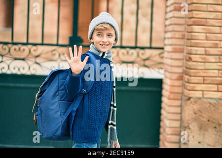 Adorable enfant blond étudiant disant Au revoir avec la main se mettre à l'école. Banque D'Images