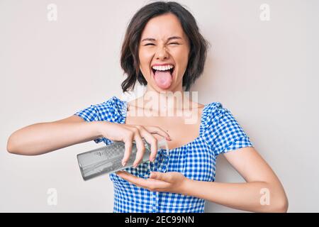 Jeune belle femme utilisant le gel désinfectant pour les mains collant la langue heureux avec l'expression drôle. Banque D'Images