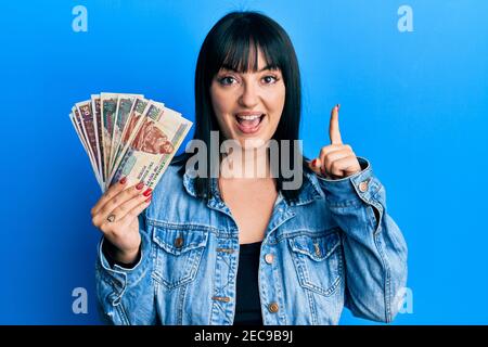 Jeune femme hispanique portant des billets en livres égyptiennes souriant avec une idée ou une question pointant du doigt avec un visage heureux, numéro un Banque D'Images