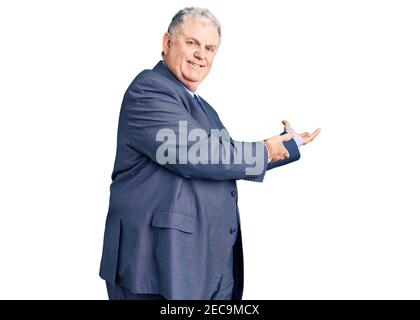 Homme aux cheveux gris senior portant une veste d'affaires invitant à entrer en souriant naturel à main ouverte Banque D'Images