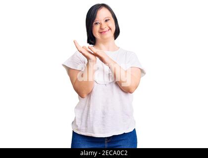 Brunette femme avec le syndrome de Down vêtu d'un chandail blanc décontracté applaudissant et applaudissant heureux et joyeux, souriant fiers mains ensemble Banque D'Images