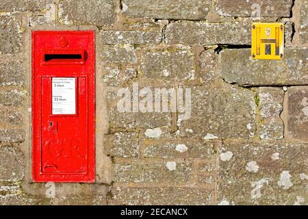 Une boîte postale britannique rouge ou une boîte postale fixée dans un mur. Il porte le chiffre de George V (1910-1936). Également un panneau jaune de borne d'incendie britannique. Banque D'Images