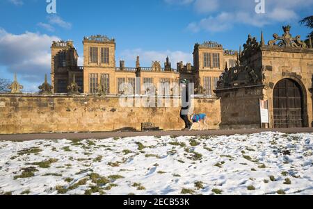 Homme avec son Whippet marchant le long d'une petite route de campagne avec de la neige en face de Hardwick Hall, Derbyshire. Banque D'Images