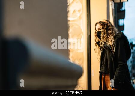 Jeune femme blonde avec masque regardant une fenêtre de magasin dans la rue. Banque D'Images