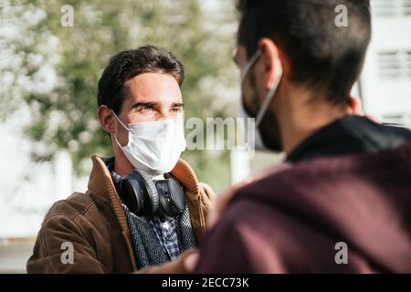 Deux hommes gais avec des masques de visage sur regarder avec amour l'un l'autre tandis que l'un touche le visage de l'autre. Banque D'Images