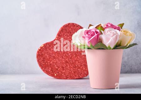 Composition festive avec de belles fleurs de roses délicates dans une boîte ronde rose avec coeur rouge sur fond gris clair. Flat lay, espace de copie. Banque D'Images