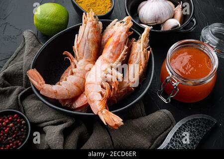 Grande coquille crue sur les grosses crevettes géantes crues dans un bol, sur fond noir Banque D'Images