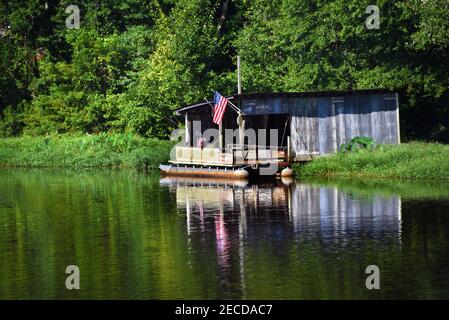 La maison de bateau rustique et la barge s'assoient sur les rives du lac White Oak dans le sud de l'Arkansas. Les drapeaux sont fièrement exposés à l'extérieur de la maison de bateau. Banque D'Images