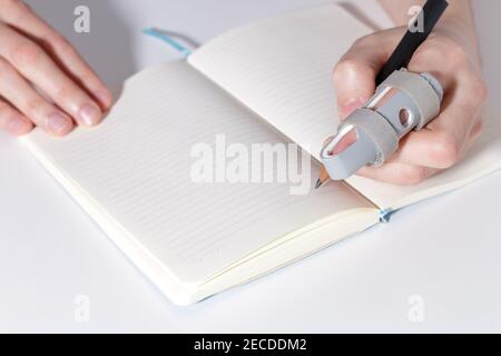 Homme gaucher avec une attelle double face en plastique gris avec deux sangles à crochet et boucle sur un index cassé, appareil médical, mains mâles écrivant dans un carnet avec un crayon noir après une blessure Banque D'Images