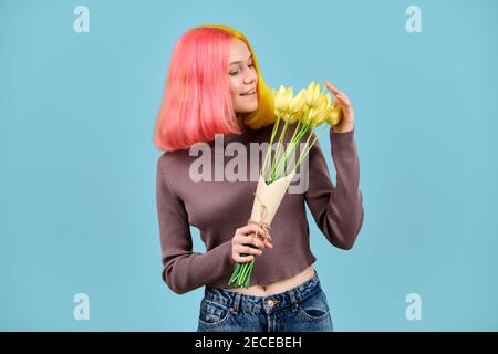 Magnifique modèle jeune souriant avec bouquet de tulipes jaunes arrière-plan bleu Banque D'Images