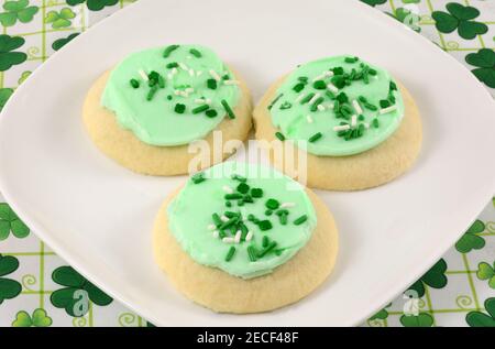Biscuits de la Saint-Patrick avec glaçage vert et saupoudrage assiette blanche sur la nappe shamrock Banque D'Images