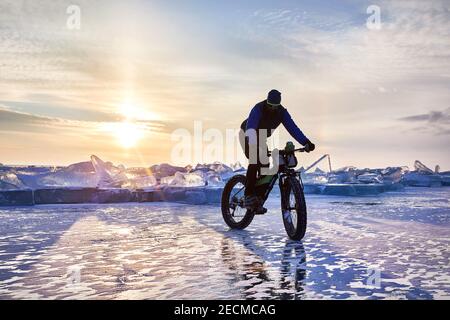 Homme faire tour à vélo gras sur le lac gelé Kapchagay au coucher du soleil au Kazakhstan Banque D'Images