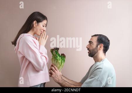Jeune homme proposant à la femme avec un bouquet de feuilles de salade, choix sain de manger. Prise de vue amusante, concept d'humour, portrait en studio, gros plan. Copier l'espace pour t Banque D'Images