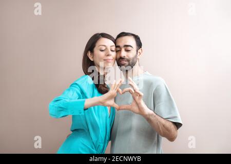 Jeune adulte heureux couple montrant la forme du cœur avec les doigts. Amour, soin. Race mixte, cheveux bruns. Des gens attrayants, portrait de gros plan. Creative studio sh Banque D'Images