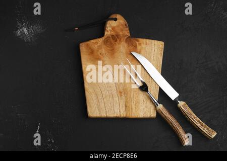 Couteau et fourchette pour steak sur planche à découper en bois vide sur fond noir Banque D'Images