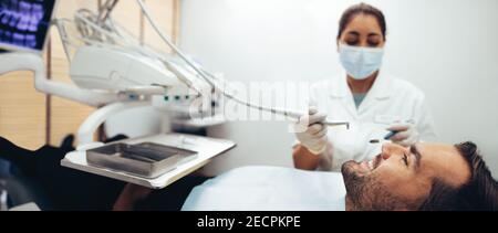 Homme souriant assis dans la chaise du dentiste recevant un traitement dentaire d'une femme dentiste. Un patient de sexe masculin obtient un examen dentaire en clinique. Banque D'Images