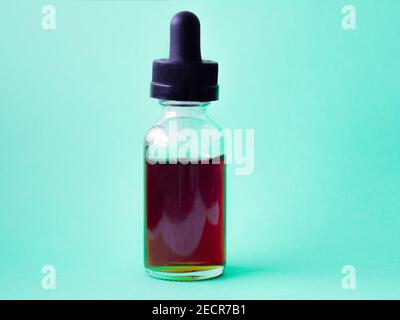 Liquide rouge foncé dans un flacon en verre avec une pipette sur fond vert vif. Une bouteille avec un liquide Banque D'Images