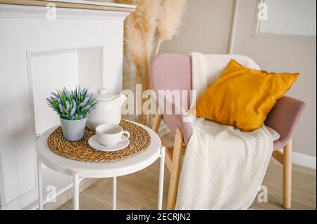 Elégant et élégant salon de composition écologique avec table de petit-déjeuner blanc café tasse théière fausse cheminée fleurs séchées plantes pampas herbe rose poudreuse fauteuil, couverture et oreiller. Décoration moderne. Banque D'Images