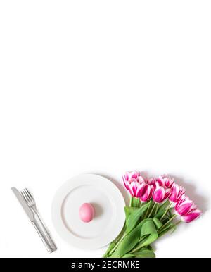 Décorations de table de Pâques avec un œuf de poulet peint en rose et un bouquet de tulipes sur fond blanc. Réglage de la barre de coupe. Format vertical. Copier l'espace. Banque D'Images