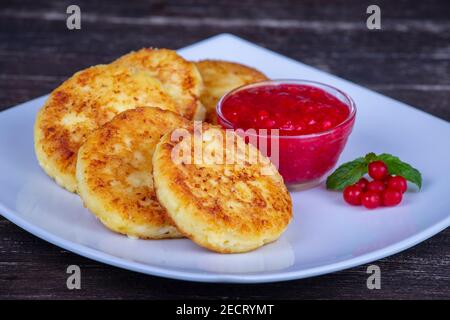 Crêpes au fromage avec confiture de baies rouges dans une assiette blanche sur une table en bois, gros plan Banque D'Images