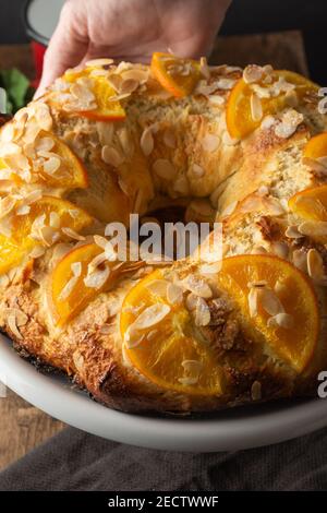 Gros plan du gâteau Kings avec des morceaux d'orange et d'amandes, fraîchement confectionnés sur une assiette blanche, sur fond sombre, à la verticale Banque D'Images