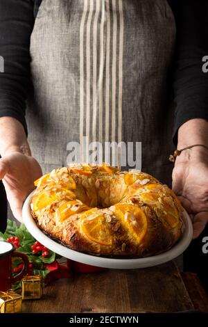Femme avec tablier gris tenant une assiette blanche avec le gâteau de Kings fraîchement fait, sur fond sombre, vertical Banque D'Images