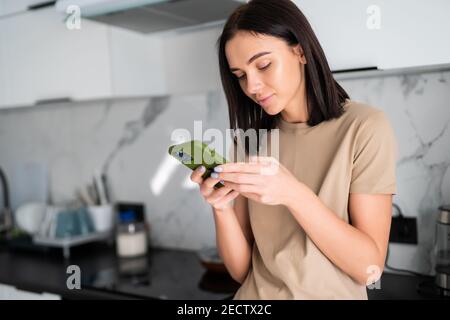 Jeune belle femme utilise le téléphone dans la cuisine. Création de contenu et communication. Banque D'Images