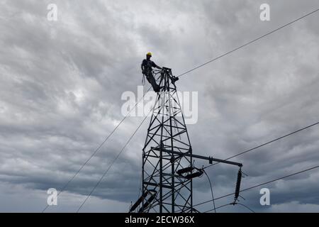 Poteaux d'escalade d'électricien, réparation de lignes électriques. Silhouette d'un ouvrier grimpant sur le poteau électrique. Réparation par un électricien du système électrique. Banque D'Images