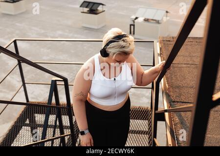 Femme de taille plus en vêtements de sport prenant une pause et vue sur un escalier Banque D'Images