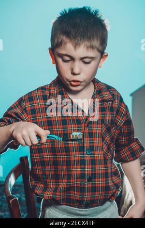 Un garçon en pyjama brosse ses dents, l'hygiène buccale de l'enfance est particulièrement importante. Le garçon avec le dégoût et la grimace au dentifrice regarde t Banque D'Images