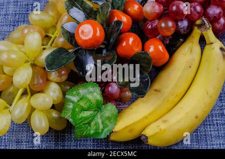 Encore la vie avec des bananes, des raisins et des mandarines décoratives. Baies et fruits en gros plan sur fond blanc et bleu. Nourriture, ingrédients. Vue latérale Banque D'Images