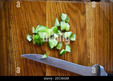 Des tranches de concombres fraîches vertes pour une salade d'été avec un couteau de cuisine en métal reposent sur un plan de cuisine en bois brun. Banque D'Images