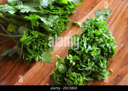 Un bouquet de persil frais lavé vert et de persil haché pour la salade sur un plan de cuisine en bois. Banque D'Images